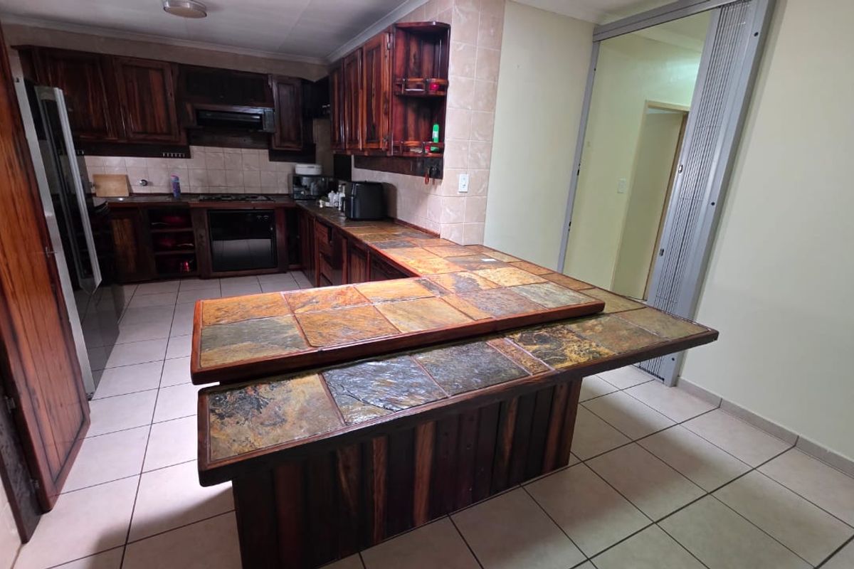 A dated kitchen featuring dark wood cabinetry, a slate-tiled breakfast bar, built-in oven, and tiled flooring, offering potential for a modern renovation.