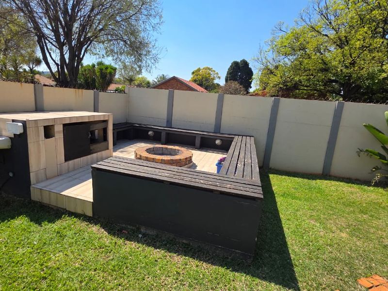 Outdoor entertainment area featuring a built-in braai, fire pit, and integrated seating, set within a private garden with a boundary wall.
