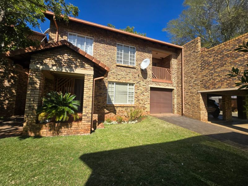 A well-maintained double-story face brick townhouse featuring a paved driveway, integrated garage, and a private balcony.
