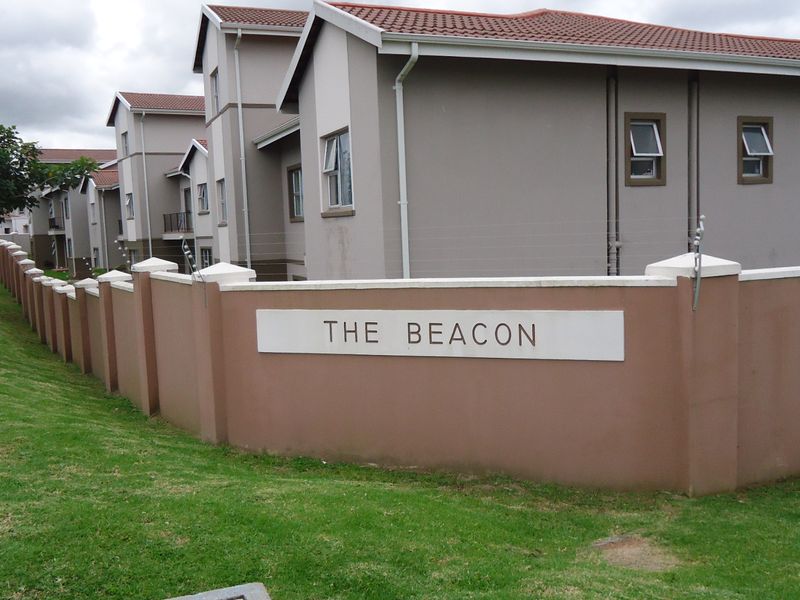 Exterior view of The Beacon apartment complex featuring a perimeter wall with electric fencing and multi-story residential units with tiled roofs.