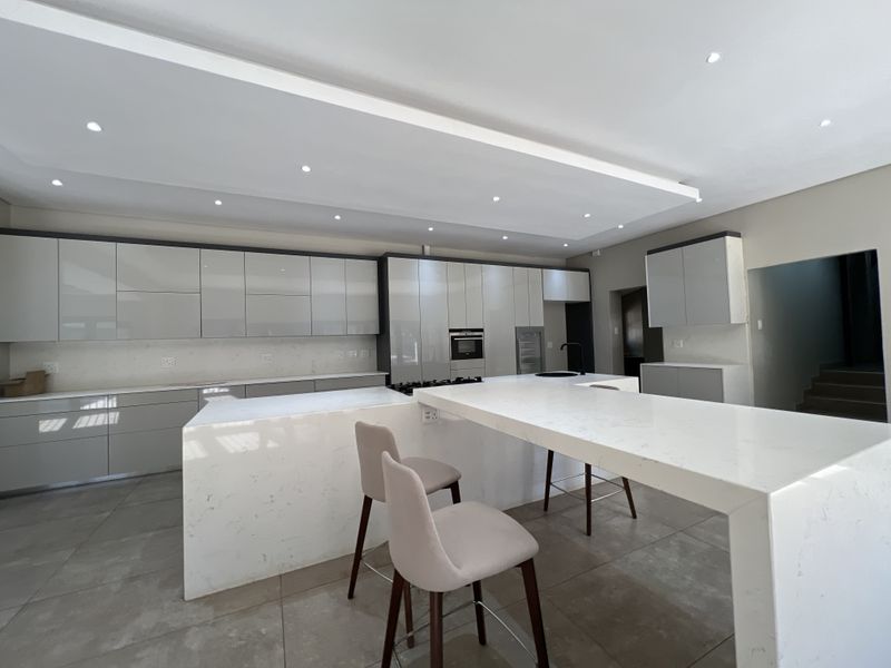 Modern kitchen featuring high-gloss cabinetry, stone countertops, a large central island with breakfast bar seating, and integrated appliances.