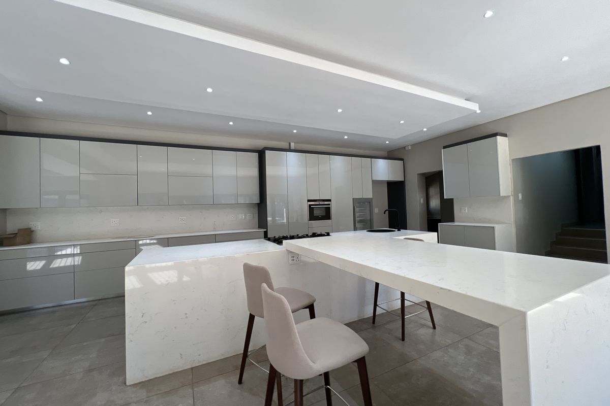 Modern kitchen featuring high-gloss cabinetry, stone countertops, a large central island with breakfast bar seating, and integrated appliances.