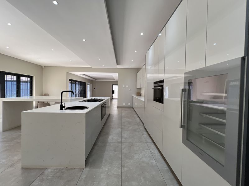 Modern, spacious kitchen featuring a large island with stone countertops, integrated appliances, high-gloss cabinetry, and sleek tiled flooring throughout.