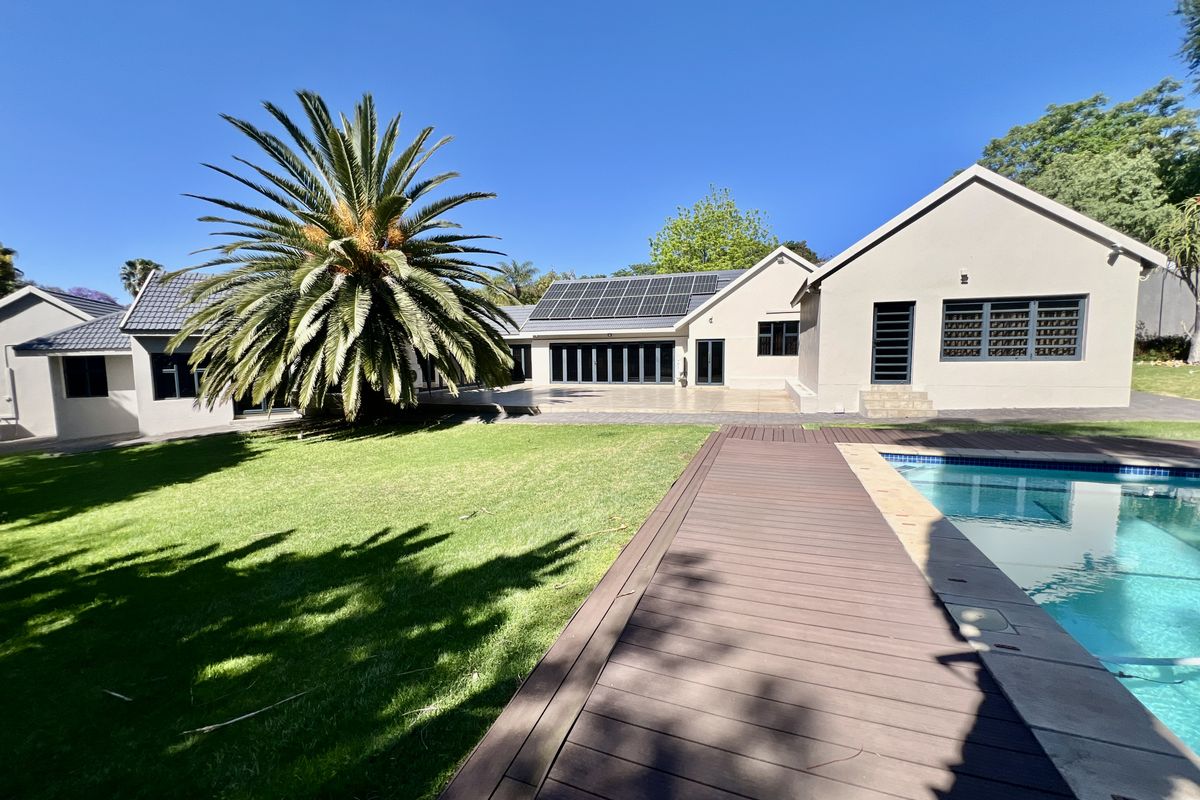 Spacious rear exterior featuring a well-maintained swimming pool, timber decking, landscaped lawn, and a modern home facade with solar panels and bi-fold doors.