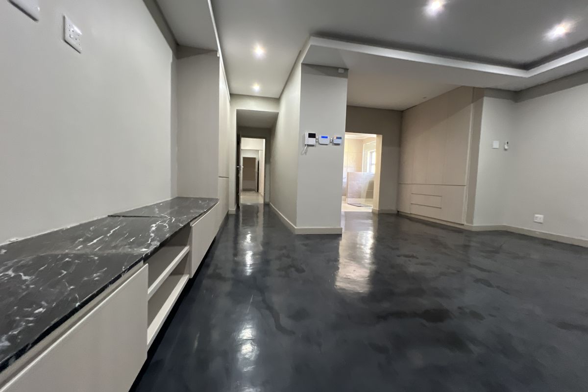 Spacious living area featuring polished concrete floors, modern built-in cabinetry with marble-look surfaces, and recessed ceiling lighting.