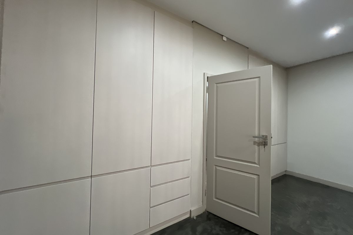 A clean, empty bedroom featuring extensive floor-to-ceiling built-in cupboards, recessed downlighting, and a neutral interior finish.