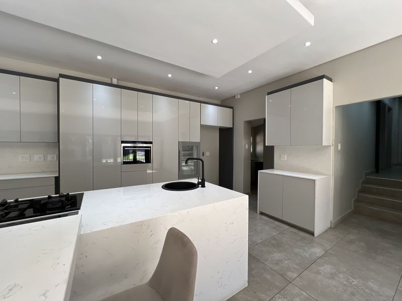 Modern kitchen featuring high-gloss cabinetry, stone countertops, a central island with a gas hob, and integrated appliances in a clean, contemporary design.