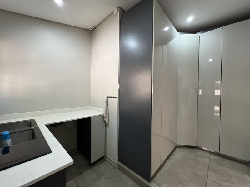 A modern, clean scullery featuring sleek high-gloss cabinetry, stone countertops, and an integrated sink, providing ample storage and functional workspace.