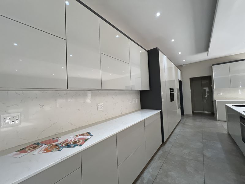 Modern kitchen featuring high-gloss cabinetry, stone countertops, marble-look backsplash, and integrated appliances with sleek tiled flooring.