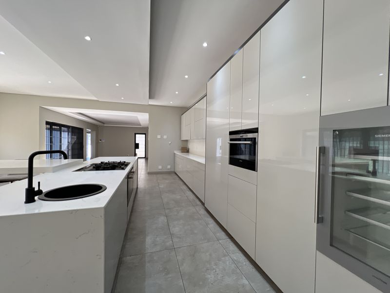 Modern, high-end kitchen featuring sleek white cabinetry, a large stone-topped island with a gas hob, integrated appliances, and contemporary recessed lighting.