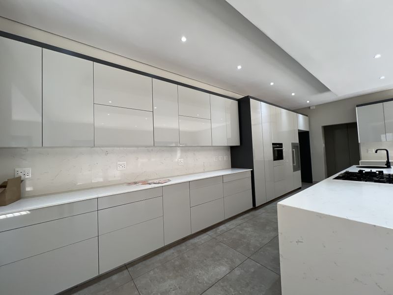Modern, high-end kitchen featuring sleek gloss cabinetry, stone countertops, marble-look splashback, integrated appliances, and large format floor tiles.