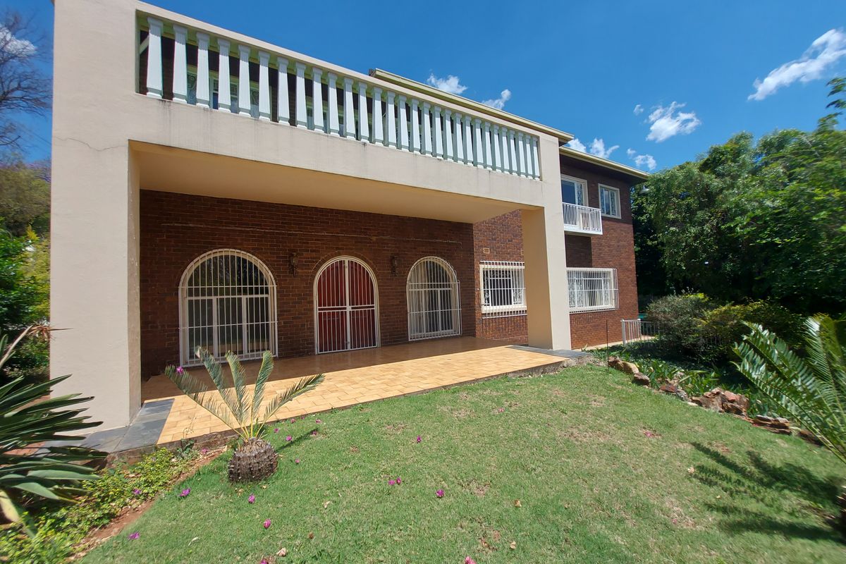Rear view of the property featuring a covered patio, brick facade, and an upper-level balcony with security features.
