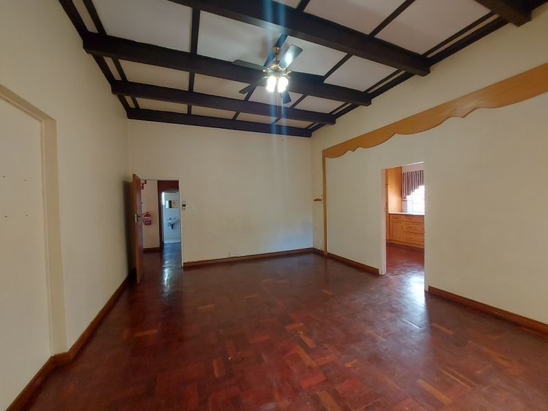 Spacious living area featuring classic parquet flooring and exposed timber ceiling beams, offering a versatile layout with direct access to adjacent rooms.
