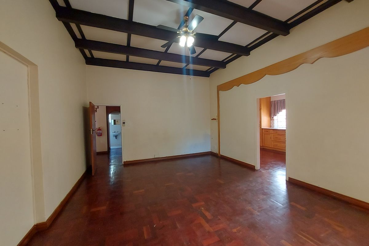 Spacious living area featuring classic parquet flooring and exposed timber ceiling beams, offering a versatile layout with direct access to adjacent rooms.