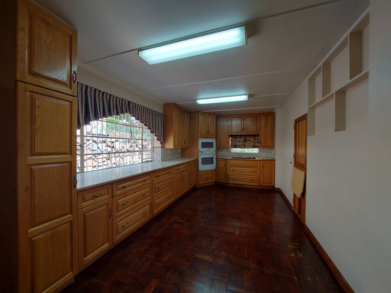 Spacious kitchen featuring extensive wooden cabinetry, built-in oven and microwave, tiled backsplash, and traditional parquet flooring, offering a functional layout with ample storage.