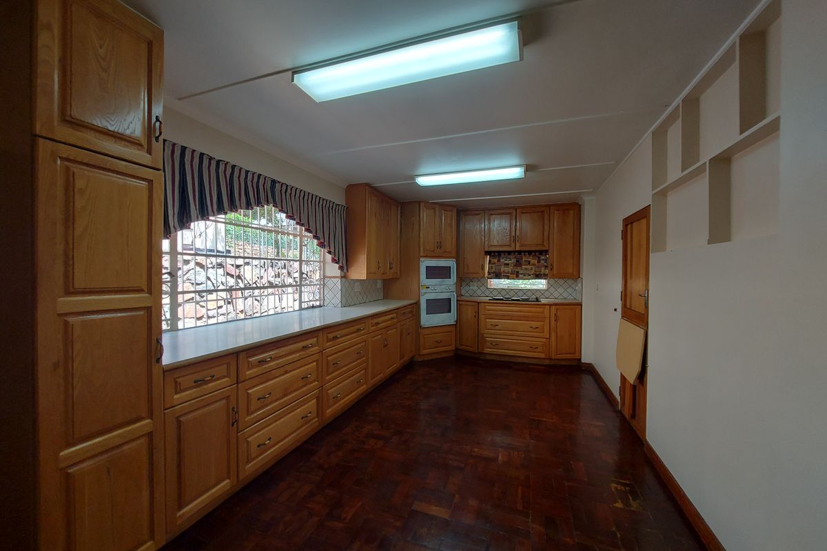 Spacious kitchen featuring extensive wooden cabinetry, built-in oven and microwave, tiled backsplash, and traditional parquet flooring, offering a functional layout with ample storage.