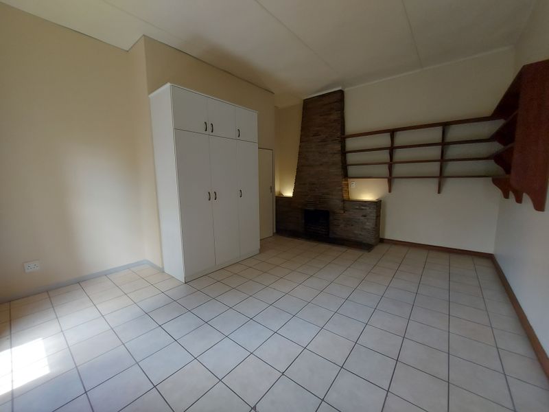 Spacious living area featuring tiled flooring, a distinctive stone-clad fireplace, and built-in storage cupboards, offering a versatile layout for comfortable family living.