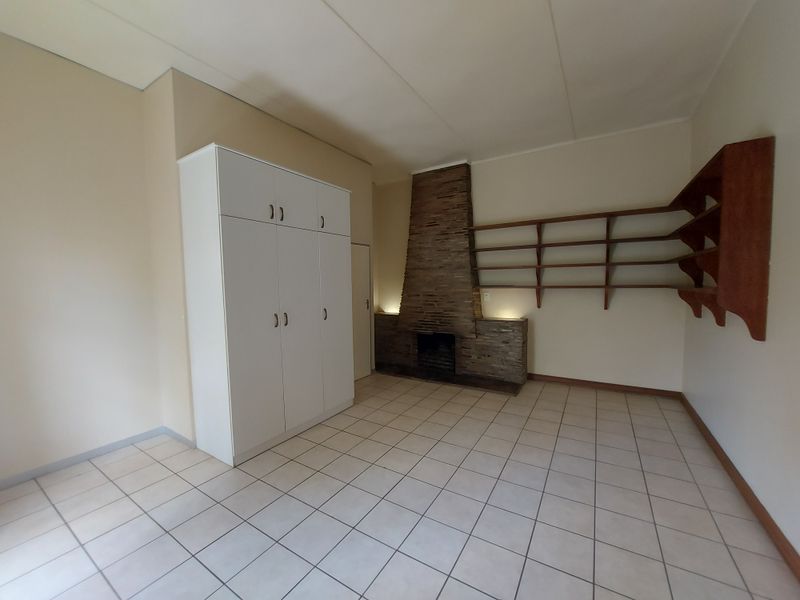 Spacious living area featuring tiled flooring, a prominent stone-clad fireplace, and built-in storage cupboards and shelving.