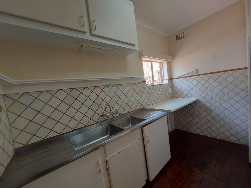 A functional kitchen space featuring a stainless steel double sink, built-in cabinetry, and tiled backsplash, offering a blank canvas for potential renovation.
