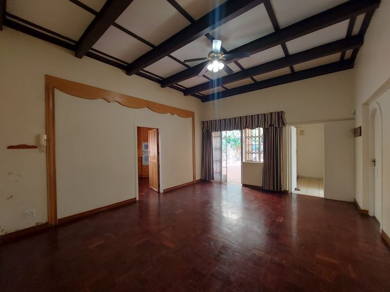 Spacious living room featuring classic parquet flooring, exposed timber ceiling beams, and direct access to the outdoor patio area.