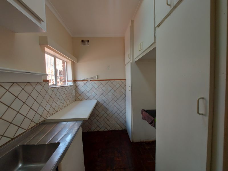 A functional scullery area featuring built-in cabinetry, a stainless steel sink, tiled splashbacks, and parquet flooring, offering a practical space for utility and prep.