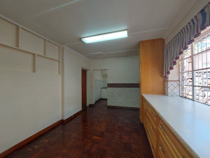An empty kitchen featuring dated wooden cabinetry, laminate countertops, parquet flooring, and a tiled splashback, offering a functional space ready for modernization.