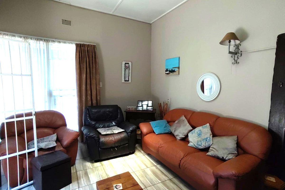 A living room featuring tiled flooring, a wall-mounted light fixture, and access to the exterior via a sliding door with a security gate.