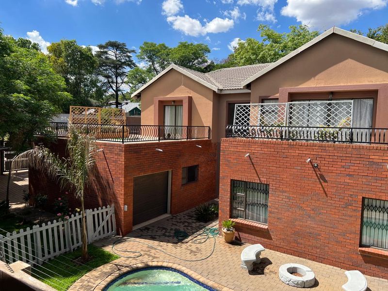 Rear view of a multi-level face brick house featuring a swimming pool, paved patio area, and upper-level balconies with metal railings.