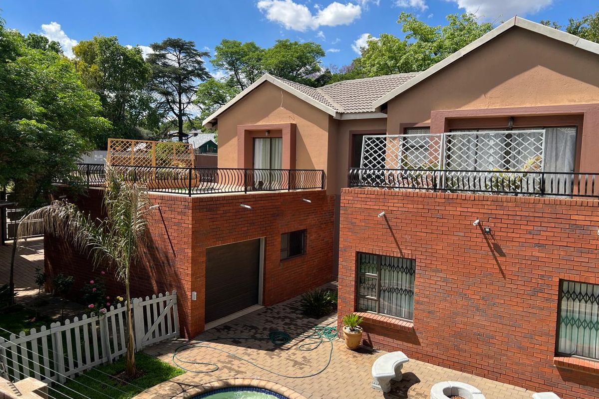 Rear view of a multi-level face brick house featuring a swimming pool, paved patio area, and upper-level balconies with metal railings.