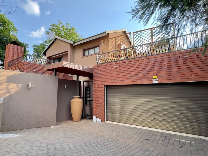 Front elevation of a multi-level house featuring a brick facade, automated garage door, paved driveway, and an upper-level balcony with metal railings.