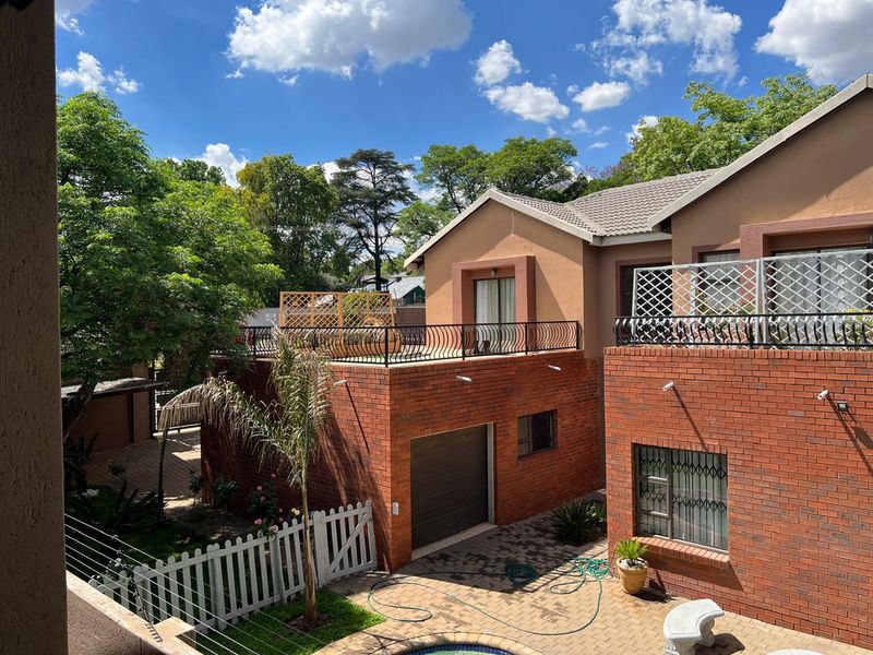 Rear view of a multi-level brick house featuring a balcony with wrought iron railings, a paved courtyard, and a swimming pool area.