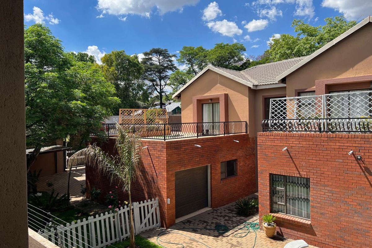 Rear view of a multi-level brick house featuring a balcony with wrought iron railings, a paved courtyard, and a swimming pool area.