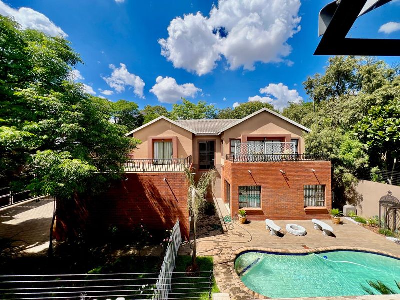 Rear view of a two-story brick house featuring a swimming pool, paved patio area, and upper-level balconies with wrought iron railings.