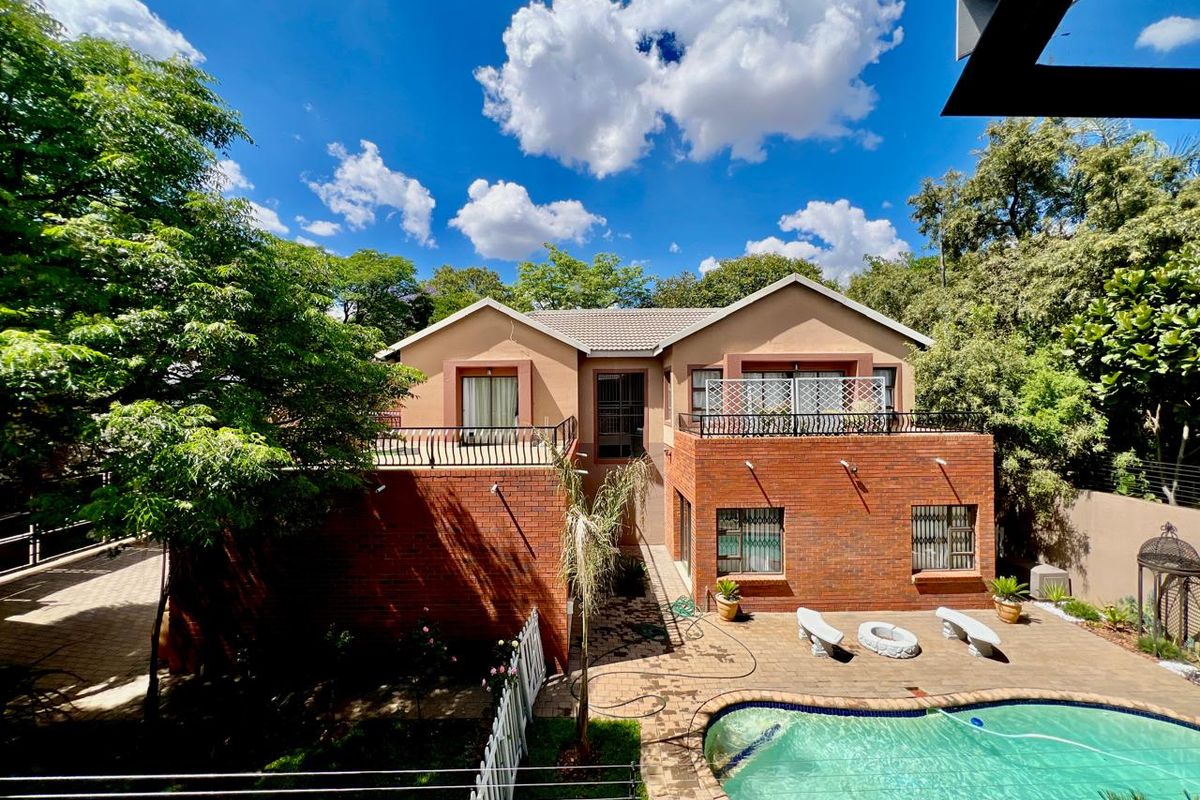 Rear view of a two-story brick house featuring a swimming pool, paved patio area, and upper-level balconies with wrought iron railings.