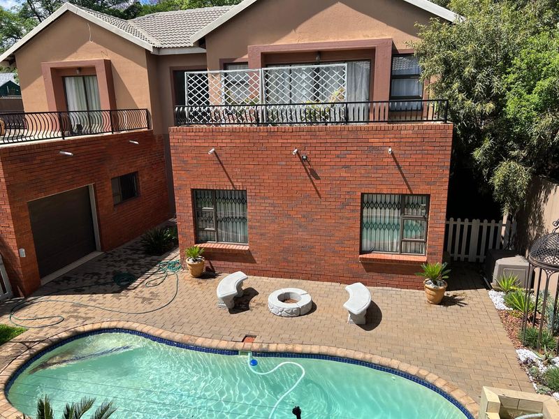 Rear exterior view featuring a paved patio area, swimming pool, and a two-story brick building with an upper-level balcony.