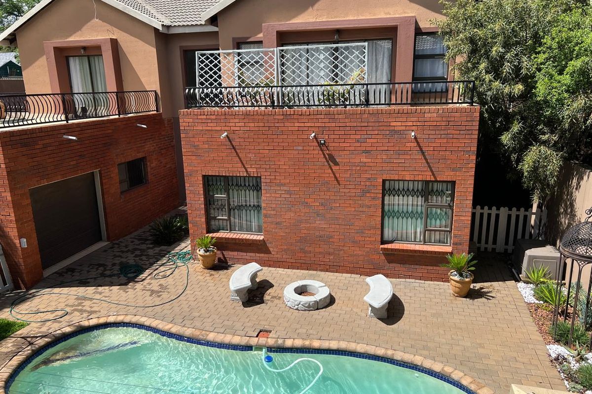 Rear exterior view featuring a paved patio area, swimming pool, and a two-story brick building with an upper-level balcony.