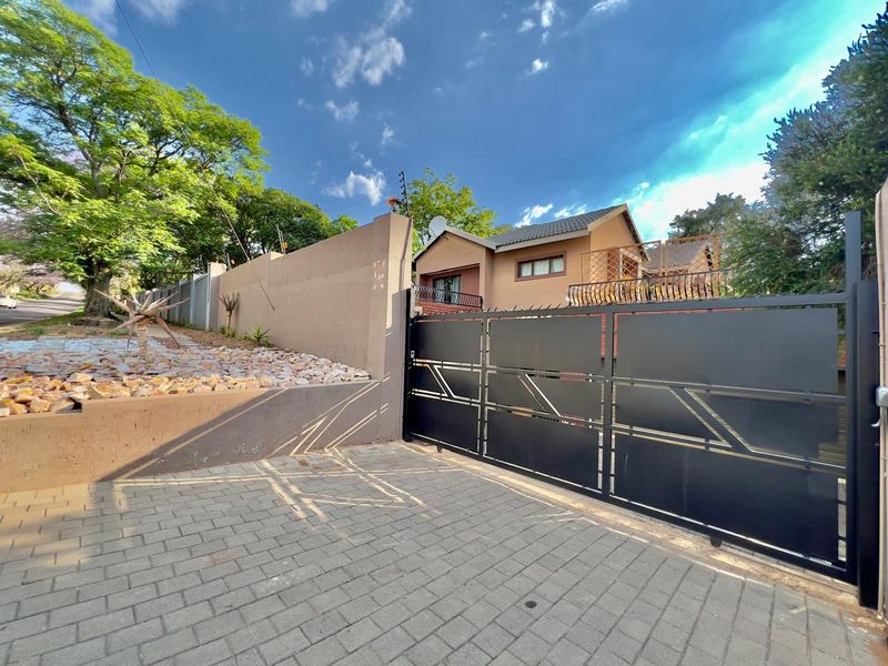 Front view of the property featuring a paved driveway, modern metal sliding gate, perimeter wall with electric fencing, and a landscaped rock garden.