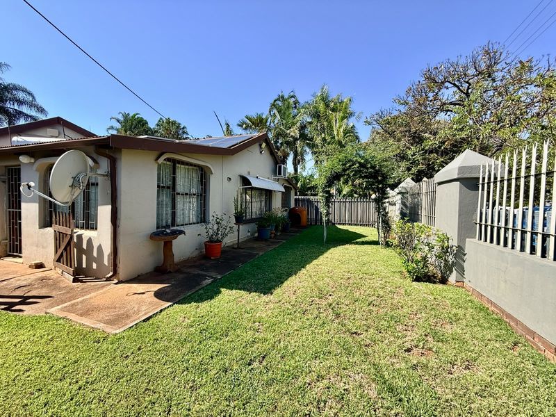 A view of the rear exterior of the house featuring a lawn, concrete pathway, security fencing, and solar panels installed on the roof.