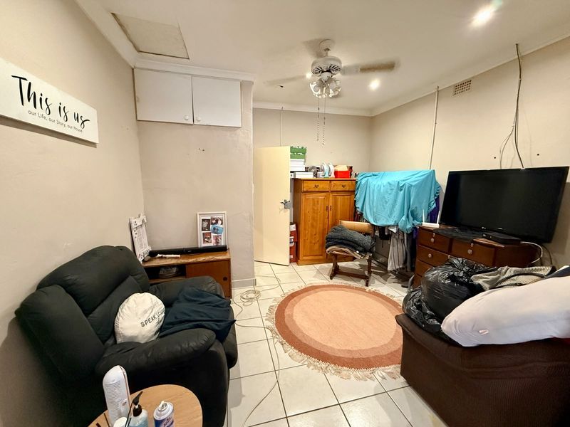 A living room featuring tiled flooring, a ceiling fan, and built-in storage cupboards, currently requiring cosmetic updates and improved cable management.