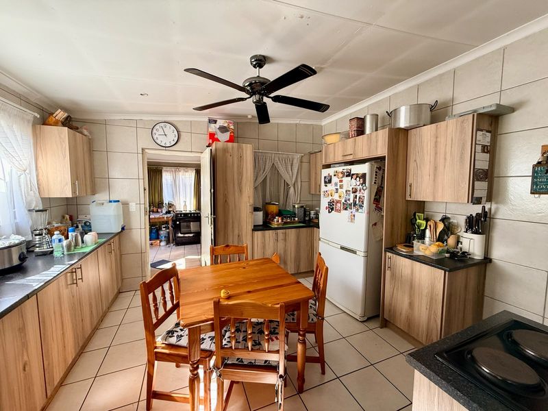 A functional kitchen featuring wood-look cabinetry, tiled walls and flooring, and a central ceiling fan, with an adjacent scullery area visible.