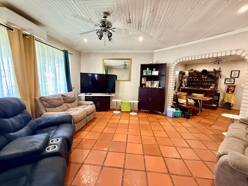 Open plan living area featuring terracotta floor tiles, a timber ceiling with fan, and a distinctive brick archway leading to an adjacent space.