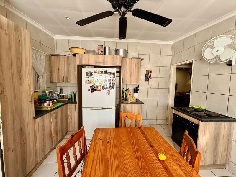 A functional kitchen featuring wood-look cabinetry, tiled walls and flooring, built-in oven and hob, and a ceiling fan for ventilation.