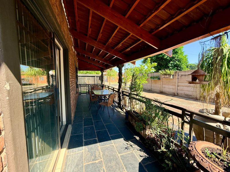 Covered patio featuring exposed timber beam ceiling, slate tile flooring, and brick wall, providing a functional outdoor living space.