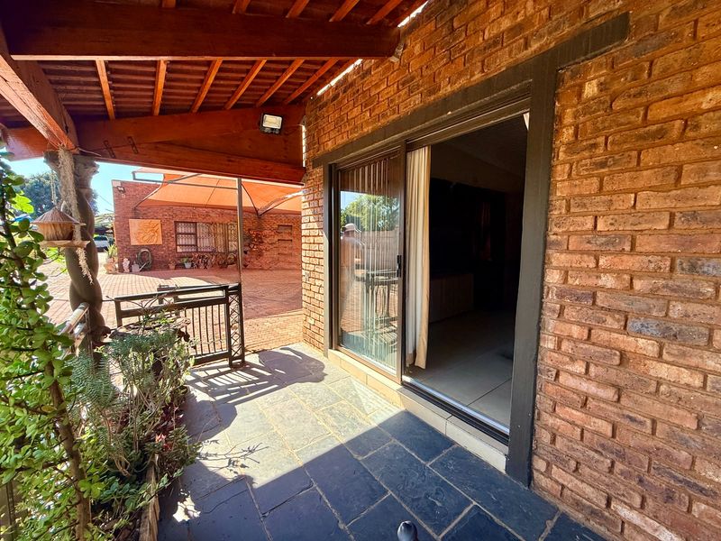 Covered patio area featuring slate flooring, exposed brickwork, and timber roof beams, providing direct access to the interior through a sliding glass door.