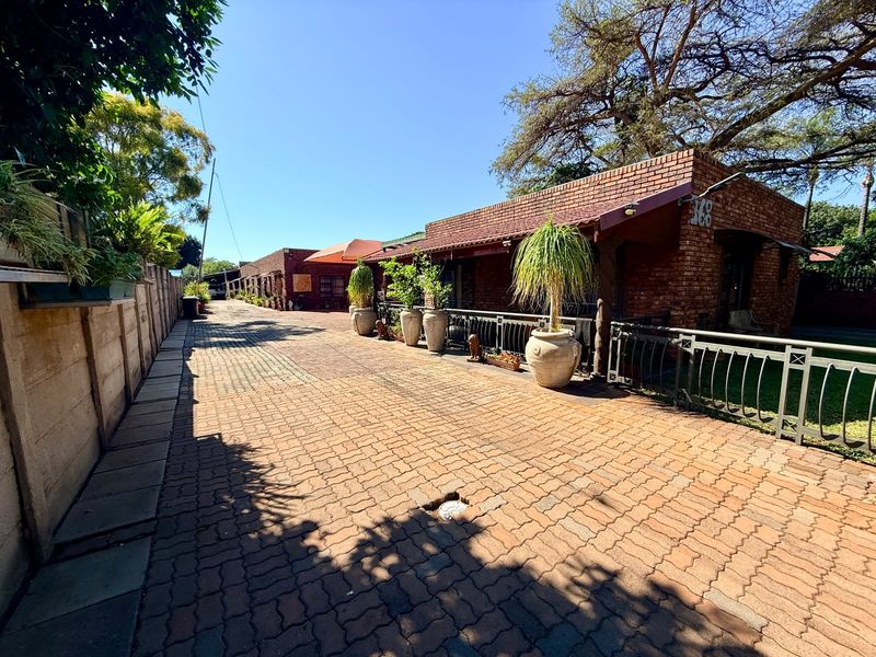 A view of the property's front exterior featuring a long paved driveway, brick facade, and secure metal fencing along the boundary.