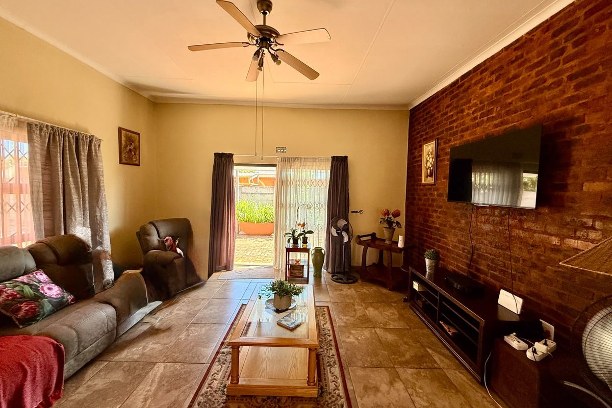 A comfortable living room featuring an exposed brick wall, tiled flooring, and a ceiling fan, with direct access to the outdoor patio area.