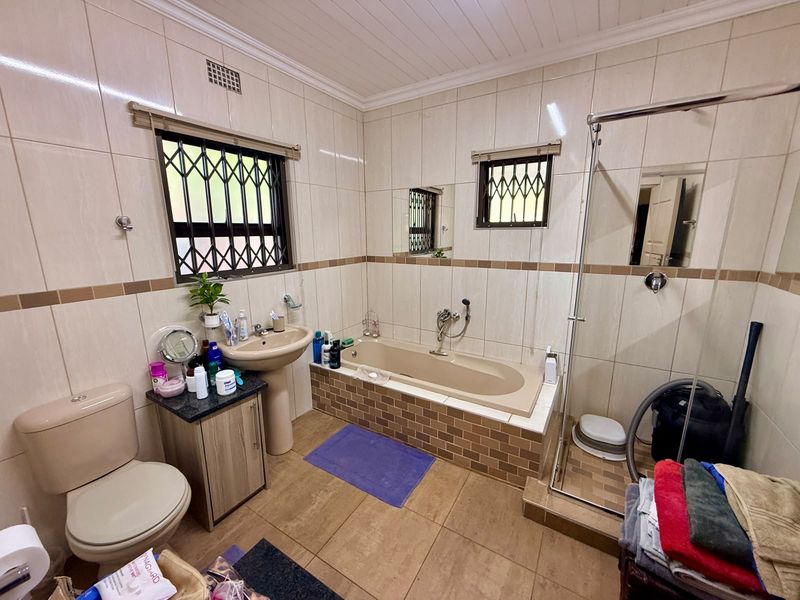 A functional bathroom featuring a built-in bathtub, separate shower enclosure, pedestal basin, and toilet with neutral wall and floor tiling.