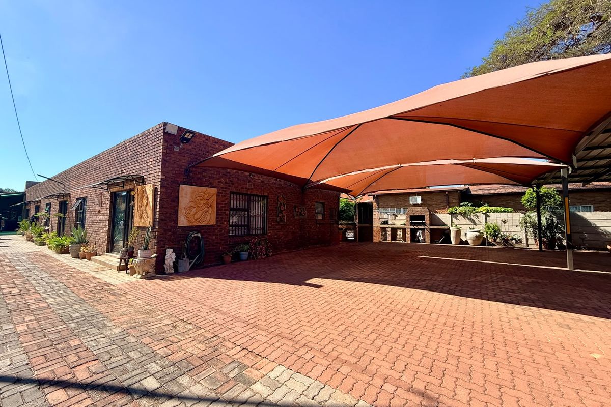 Spacious rear exterior area featuring extensive brick paving, a large shade sail covering, and a built-in braai area against a brick facade.