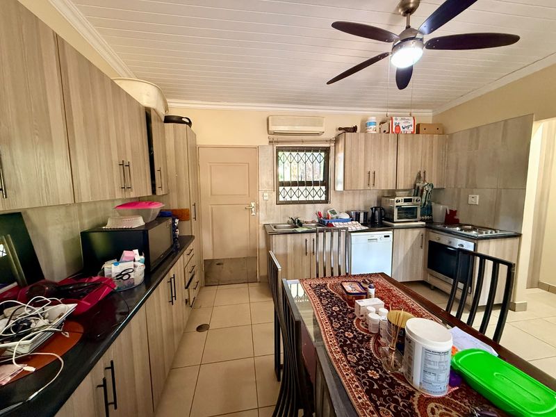 A functional kitchen featuring wood-look cabinetry, tiled flooring, built-in oven and hob, and a ceiling fan, offering a practical layout for daily meal preparation.