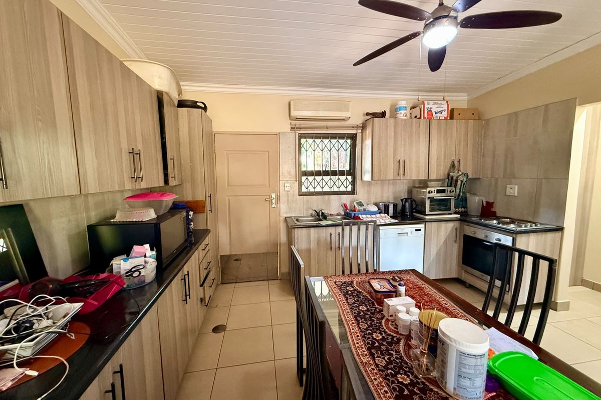 A functional kitchen featuring wood-look cabinetry, tiled flooring, built-in oven and hob, and a ceiling fan, offering a practical layout for daily meal preparation.